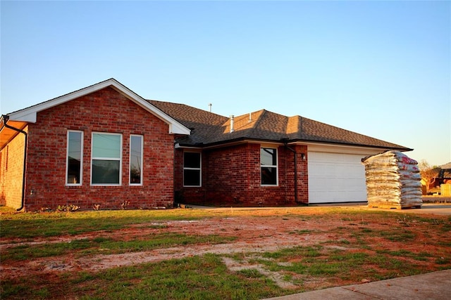 ranch-style home with a garage, driveway, a front yard, brick siding, and roof with shingles