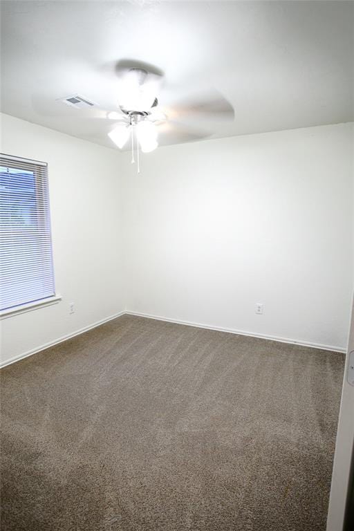spare room featuring dark carpet, baseboards, a ceiling fan, and visible vents