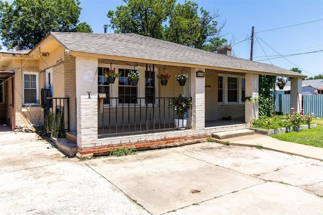 bungalow-style home featuring a chimney, fence, roof with shingles, covered porch, and brick siding