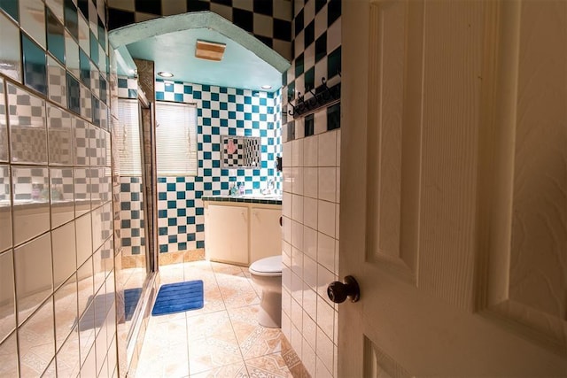 bathroom featuring a shower stall, toilet, tile patterned flooring, and tile walls