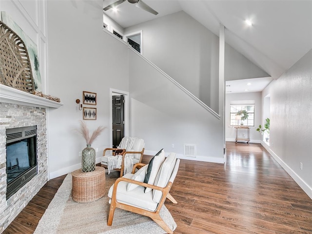 sitting room featuring wood finished floors, ceiling fan, a stone fireplace, visible vents, and high vaulted ceiling