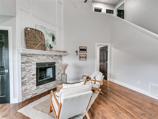 living area featuring a high ceiling, a fireplace, visible vents, baseboards, and wood finished floors
