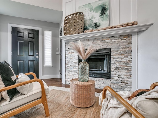 living area featuring a stone fireplace, wood finished floors, and baseboards