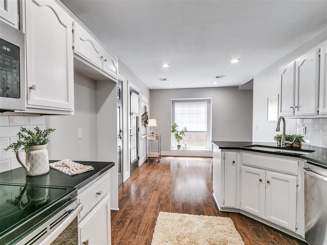 kitchen featuring white cabinets, stainless steel appliances, dark countertops, and a sink