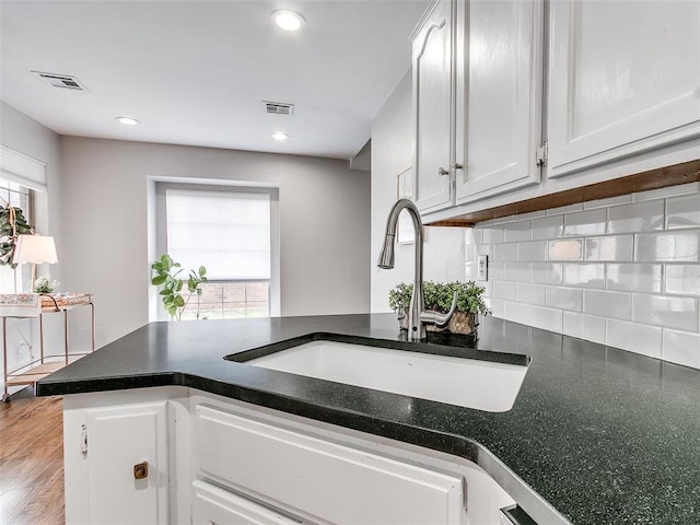 kitchen with dark countertops, a sink, white cabinetry, and decorative backsplash