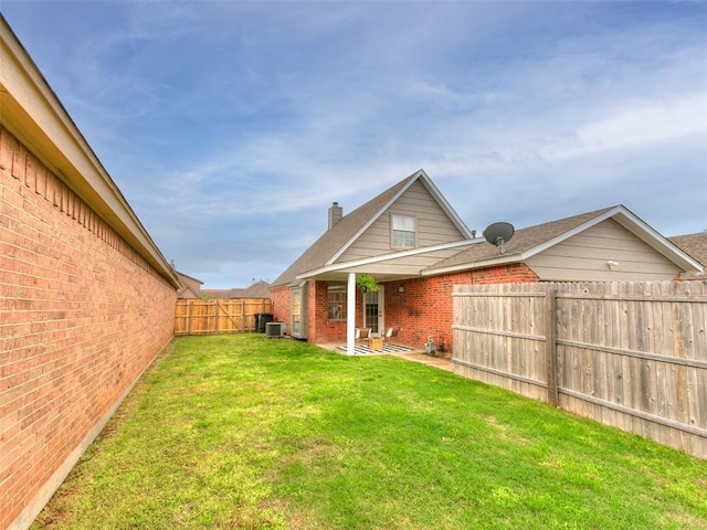 back of property featuring a chimney, a fenced backyard, brick siding, central air condition unit, and a lawn