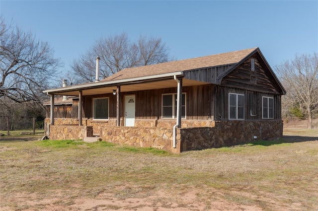 view of front of home with roof with shingles, stone siding, a front yard, and covered porch