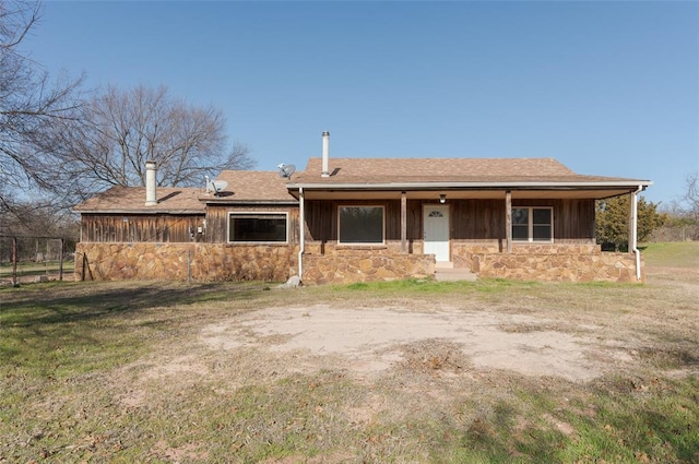 view of front of property featuring stone siding, a shingled roof, a front lawn, and a porch