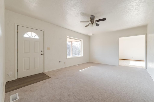 foyer entrance featuring a textured ceiling, carpet, visible vents, and ceiling fan