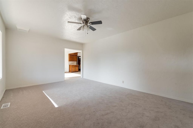 spare room with carpet, visible vents, a ceiling fan, and baseboards