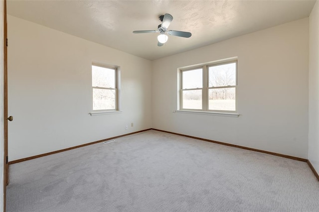 spare room with light colored carpet, baseboards, and a ceiling fan