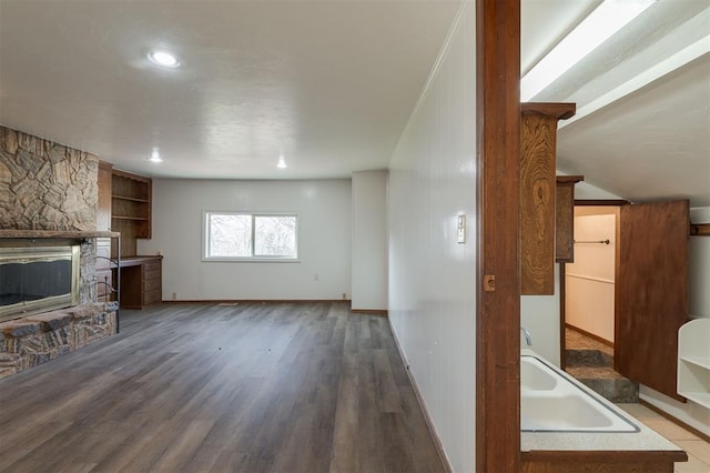 unfurnished living room featuring a stone fireplace, baseboards, wood finished floors, and a sink
