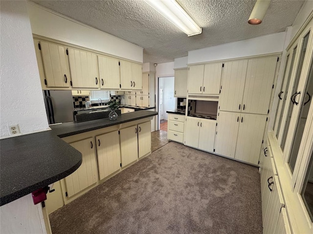608 Roosevelt St, Seminole, OK 74868 - kitchen featuring dark countertops, carpet floors, a peninsula, a textured ceiling, and cream cabinets