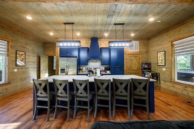 66 Morning Pines Trl, Broken Bow, OK 74728 - kitchen with a large island, visible vents, stainless steel fridge with ice dispenser, premium range hood, and wooden walls