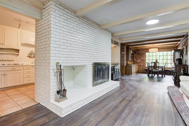 living area with brick wall, beamed ceiling, wood finished floors, and a brick fireplace