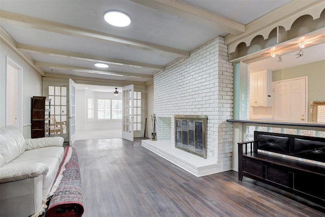 living room featuring beamed ceiling, dark wood-style flooring, a brick fireplace, and baseboards