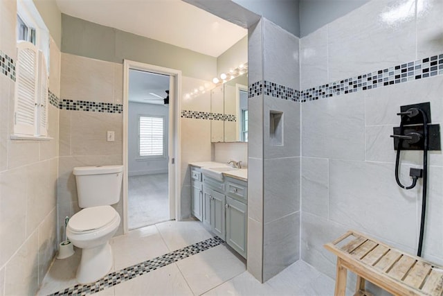 bathroom with tiled shower, tile patterned flooring, tile walls, toilet, and vanity