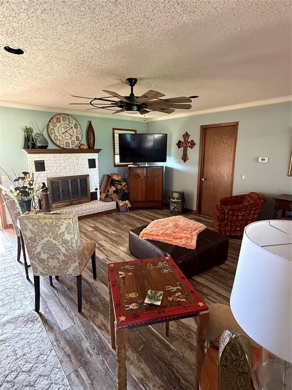 4108 N Broadway Ave, Hinton, OK 73047 - living area featuring a textured ceiling, wood finished floors, a ceiling fan, and a brick fireplace