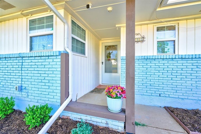 doorway to property featuring board and batten siding, brick siding, and covered porch
