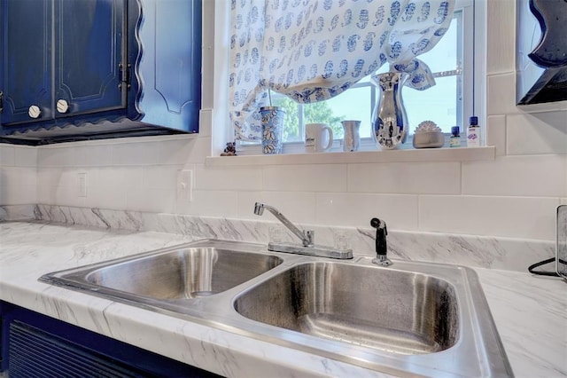 details with light stone counters, blue cabinetry, decorative backsplash, and a sink
