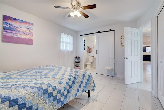 bedroom featuring a barn door, ensuite bath, ceiling fan, and light tile patterned floors