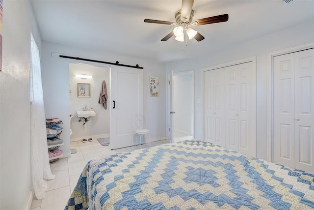 bedroom featuring a barn door, tile patterned flooring, ceiling fan, multiple closets, and ensuite bath