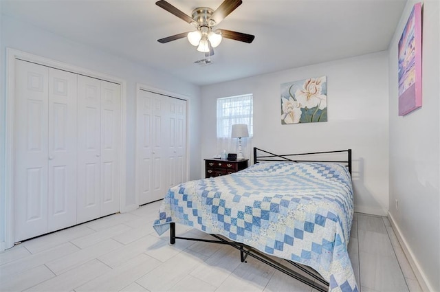 bedroom featuring two closets, visible vents, a ceiling fan, and baseboards