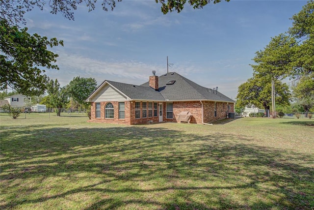 rear view of property with a chimney, fence, roof with shingles, a lawn, and brick siding