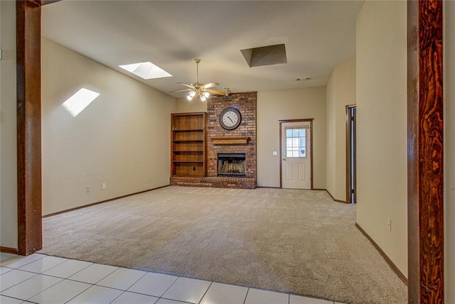 unfurnished living room featuring baseboards, light colored carpet, a skylight, a ceiling fan, and a brick fireplace