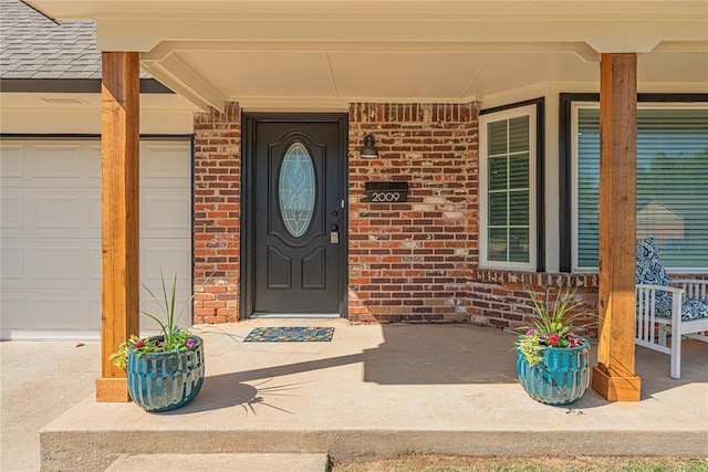 property entrance featuring an attached garage, brick siding, a porch, and roof with shingles