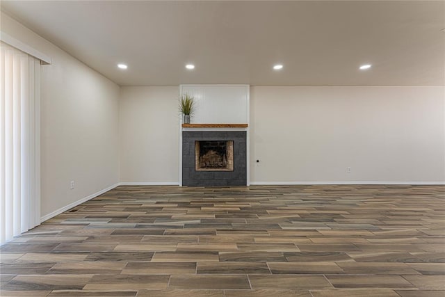 unfurnished living room with a tile fireplace, baseboards, wood finished floors, and recessed lighting