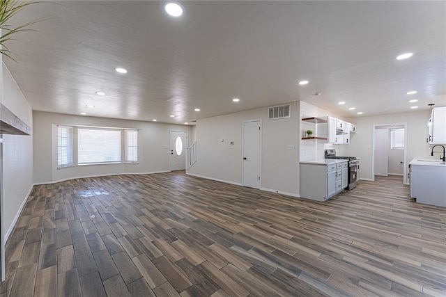 unfurnished living room featuring recessed lighting, visible vents, dark wood-style floors, and a sink