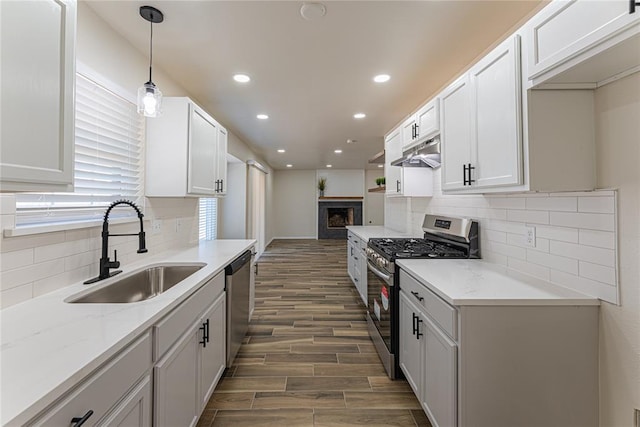 kitchen featuring under cabinet range hood, wood finished floors, a sink, tasteful backsplash, and appliances with stainless steel finishes