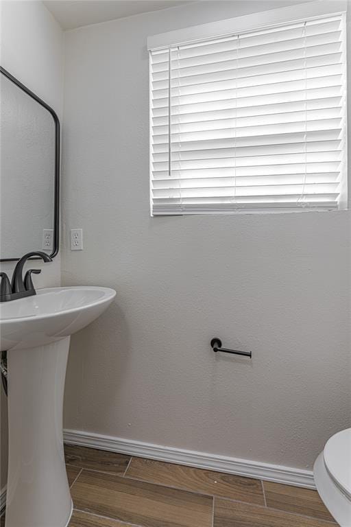 half bath with baseboards, toilet, wood finished floors, and a sink