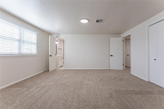 unfurnished bedroom featuring ensuite bath, light carpet, visible vents, and baseboards