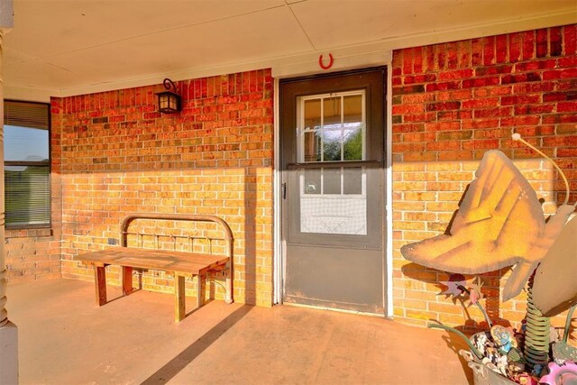 view of exterior entry with brick siding and a porch
