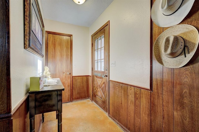 doorway with concrete flooring, a wainscoted wall, and wood walls
