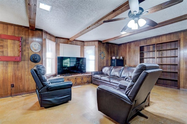 living area with ceiling fan, beamed ceiling, a textured ceiling, and wooden walls