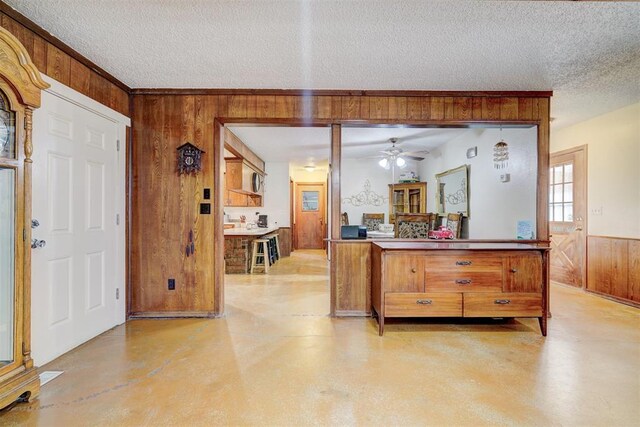 interior space with brown cabinets, wood walls, a ceiling fan, finished concrete floors, and a textured ceiling