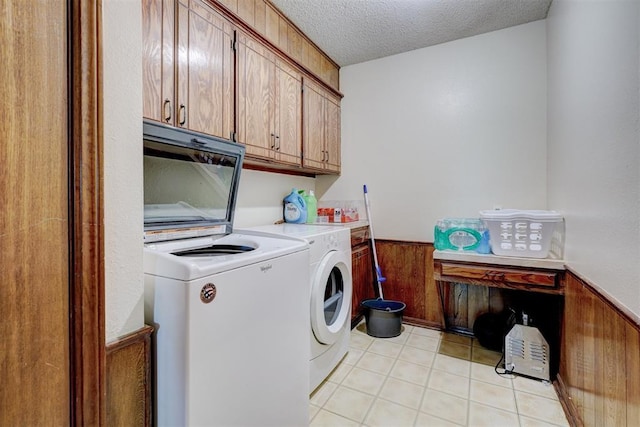 clothes washing area with a textured ceiling, wainscoting, cabinet space, wooden walls, and washer and dryer