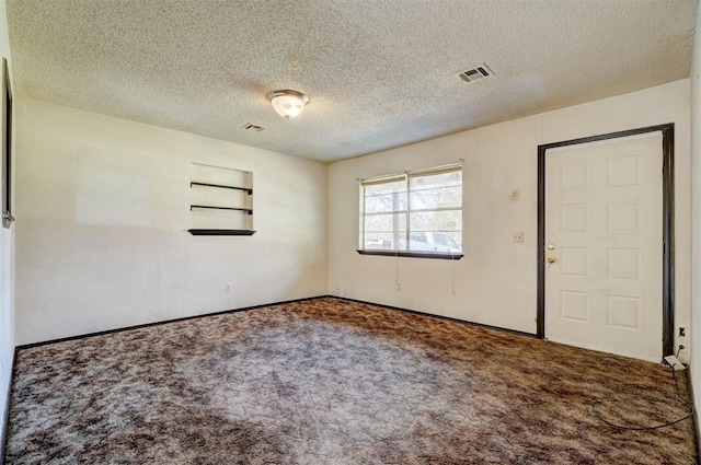 carpeted spare room featuring a textured ceiling, visible vents, and baseboards