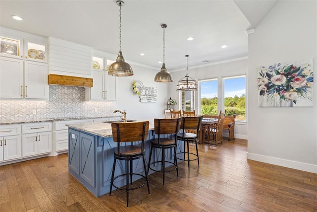 kitchen featuring a sink, a kitchen island with sink, white cabinetry, decorative backsplash, and baseboards