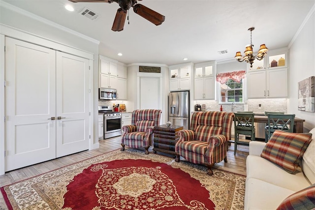 living area with crown molding, light wood-style flooring, visible vents, and ceiling fan with notable chandelier