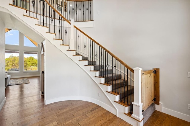stairway featuring a towering ceiling, baseboards, and wood finished floors