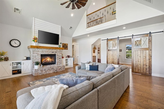 living room with a ceiling fan, hardwood / wood-style floors, a barn door, and high vaulted ceiling