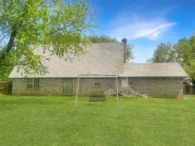rear view of house with a yard, brick siding, fence, and a chimney