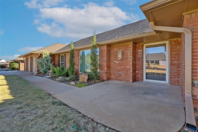 12600 Green Valley Dr, Oklahoma City, OK 73120 - exterior space featuring brick siding, a patio area, an attached garage, and roof with shingles