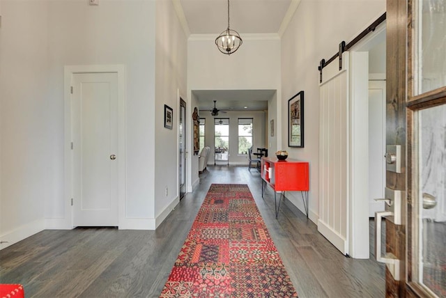 hallway with a barn door, baseboards, dark wood finished floors, a high ceiling, and ornamental molding
