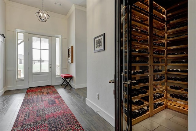 wine area with wood finished floors, a chandelier, baseboards, ornamental molding, and visible vents