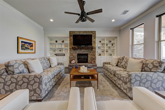 living area with a stone fireplace, visible vents, a ceiling fan, crown molding, and built in features